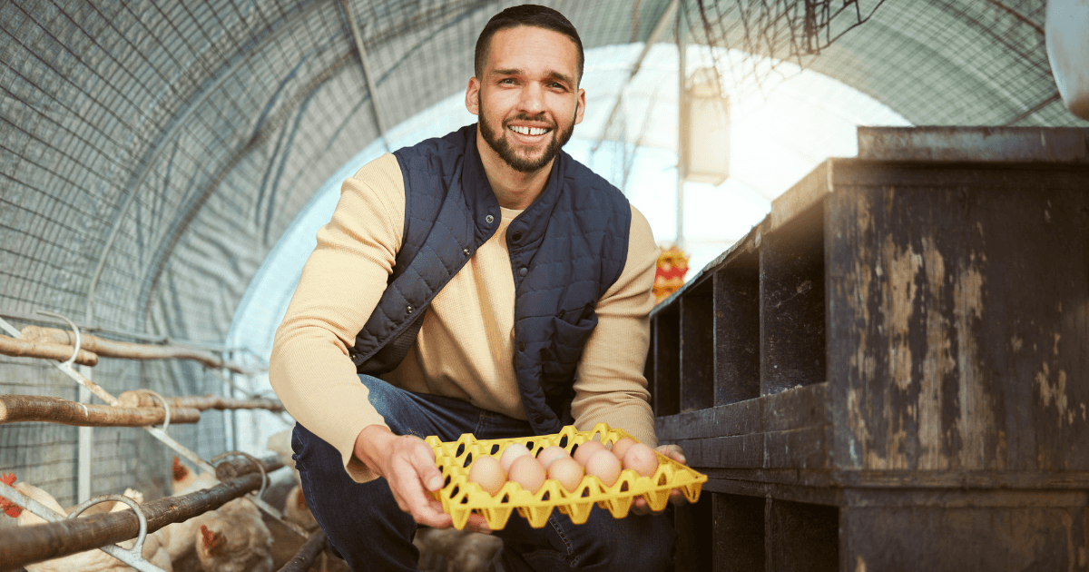 Farmer in chicken coop smiling with freshly collected eggs